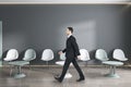 Attractive european businessman walking in modern waiting area interior with seats and wooden flooring. Policlinic and appointment