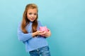 Attractive european girl holding a piggy bank in her hands on a light blue wall with copyspace Royalty Free Stock Photo