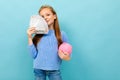 Attractive european girl holding a piggy bank and money in hands on a light blue background Royalty Free Stock Photo