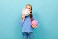 Attractive european girl holding a piggy bank and money in hands on a light blue wall Royalty Free Stock Photo