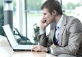 Attractive european guy talking on phone while using laptop. Royalty Free Stock Photo