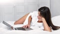 Attractive European woman enjoying weekend lying on bed in bedroom and using laptop touchpad