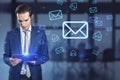 Attractive europeaqn businessman using tablet with glowing email letter icons on blurry office interior background. Communication Royalty Free Stock Photo