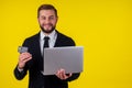 Attractive excited young brunette man isolated over yellow background holding laptop computer and plastic credit card Royalty Free Stock Photo