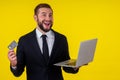 Attractive excited young brunette man isolated over yellow background holding laptop computer and plastic credit card Royalty Free Stock Photo