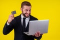 Attractive excited young brunette man isolated over yellow background holding laptop computer and plastic credit card Royalty Free Stock Photo