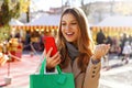 Attractive excited young woman watching smartphone and holding shopping bags walking in the Christmas Markets Royalty Free Stock Photo