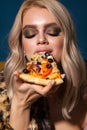 Attractive fashion model with blond hair, trendy colorful smokey eyes eatting pizza. Fur leopard coat. Blue background. Royalty Free Stock Photo