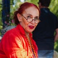 Attractive fashionable woman of 75 in red clothes sitting and roundly eyeglasses in a summer park