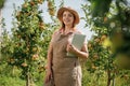 Attractive female agronomist or farmer with laptop standing in apple orchard and checking fruit, makes notes. Agriculture and Royalty Free Stock Photo