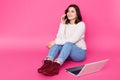 Attractive female with beautiful smile sits on floor at home, speaks on mobile phone. Beautiful girl works online using laptop, Royalty Free Stock Photo