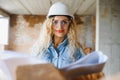 Attractive female construction worker in hardhat. Confident young specialist in checkered blue shirt in jeans standing Royalty Free Stock Photo