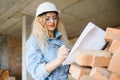 Attractive female construction worker in hardhat. Confident young specialist in checkered blue shirt in jeans standing Royalty Free Stock Photo