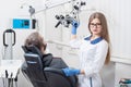 Attractive female dentist with microscope getting ready for dental procedure with male patient in modern dental office Royalty Free Stock Photo