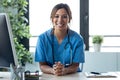 Attractive female doctor smiling looking at camera while working with laptop in the consultation Royalty Free Stock Photo