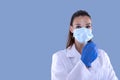 Attractive female doctor with virus protection mask and latex gloves looking straight ahead and blue background