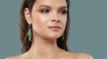 Attractive female face close up. Glamorous woman with natural shiny clean skin wearing jewelry earring with green precious stones