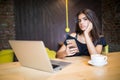 Attractive female freelancer hold smart phone while sitting at wooden table front open computer in modern coffee shop. young creat Royalty Free Stock Photo