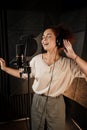 Attractive female musician in headphones emotionally singing in recording studio