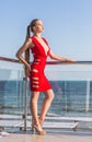 An attractive female posing on a balcony. A woman with long hair on a blue sky background. A lady in a bright red dress. Royalty Free Stock Photo