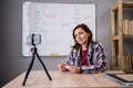 Attractive female teacher explaining and giving online lesson for students, sitting at desk, filming her vlog. Recording Royalty Free Stock Photo