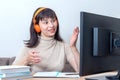 An attractive female teacher in orange headphones sitting in front of a computer monitor, explains an online task