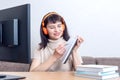 An attractive female teacher in orange headphones sitting in front of a computer monitor, explains an online task