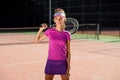 Attractive female tennis player in uniform with tennis racket walking on the outdoor tennis court at sunset background. Royalty Free Stock Photo