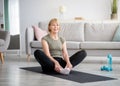 Attractive fit mature lady sitting in butterfly yoga pose on sports mat at home, copy space. Active lifestyle concept