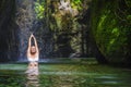 Attractive and fit tourist Caucasian woman practicing yoga exercise pose in amazing tropical exotic waterfall lagoon with green tu