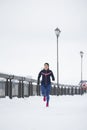 Attractive fitness female model running at snow winter park, pink sneakers Royalty Free Stock Photo