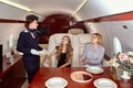 Attractive flight attendant is serving passengers of first class inside airplane. Royalty Free Stock Photo