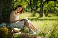 Attractive foxy woman reading book sitting in garden with her back close to tree. Royalty Free Stock Photo