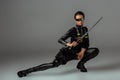 Futuristic african american woman in glasses sitting with sword on grey Royalty Free Stock Photo