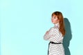 Ginger female in jewelry and light dress with black belt. She is smiling and looking back. Posing on turquoise studio background Royalty Free Stock Photo