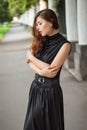 Attractive girl in a black dress with a corset on a background of a fence with clones. Evening walk on the city street.