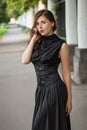 Attractive girl in a black dress with a corset on a background of a fence with clones. Evening walk on the city street.