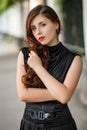 Attractive girl in a black dress with a corset on a background of a fence with clones. Evening walk on the city street.