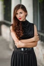 Attractive girl in a black dress with a corset on a background of a fence with clones. Evening walk on the city street.