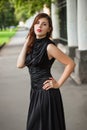 Attractive girl in a black dress with a corset on a background of a fence with clones. Evening walk on the city street.