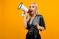 Attractive girl in a blouse shouting news in a megaphone on a yellow studio background
