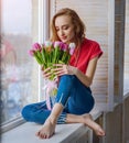 Attractive girl with bouquet of tulips on window-sill Royalty Free Stock Photo