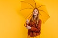 Attractive girl, in a bright yellow dress and autumn jacket, stands with a yellow umbrella on an  yellow background. Royalty Free Stock Photo