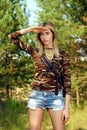 Attractive girl in camo shirt, jeans shorts with backpack on hiking trail in forest Royalty Free Stock Photo