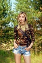 Attractive girl in camo shirt, jeans shorts with backpack on hiking trail in forest Royalty Free Stock Photo