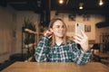 Attractive girl in casual clothing and glasses takes selfie in a coffee shop. Happy girl uses a smartphone a cozy cafe, looks at Royalty Free Stock Photo