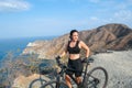 Attractive girl cyclist looking at the horizon next to a black mountain bike, enjoying a summer day in the mountains. Outdoor Royalty Free Stock Photo