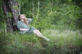 Attractive girl in the forest in a dress sits under a tree in the grass Royalty Free Stock Photo