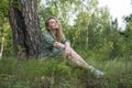 Attractive girl in the forest in a dress sits under a tree in the grass Royalty Free Stock Photo