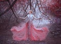 Attractive girl with gorgeous blond hairdo in the forest near the branches of trees, dressed in a light amazing pink